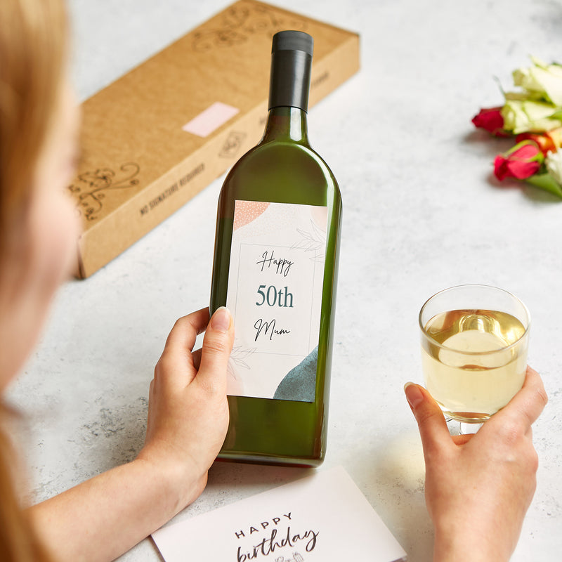 A person holding a letterbox-friendly wine bottle with personalised 'happy 50th mum' label and happy birthday greetings card