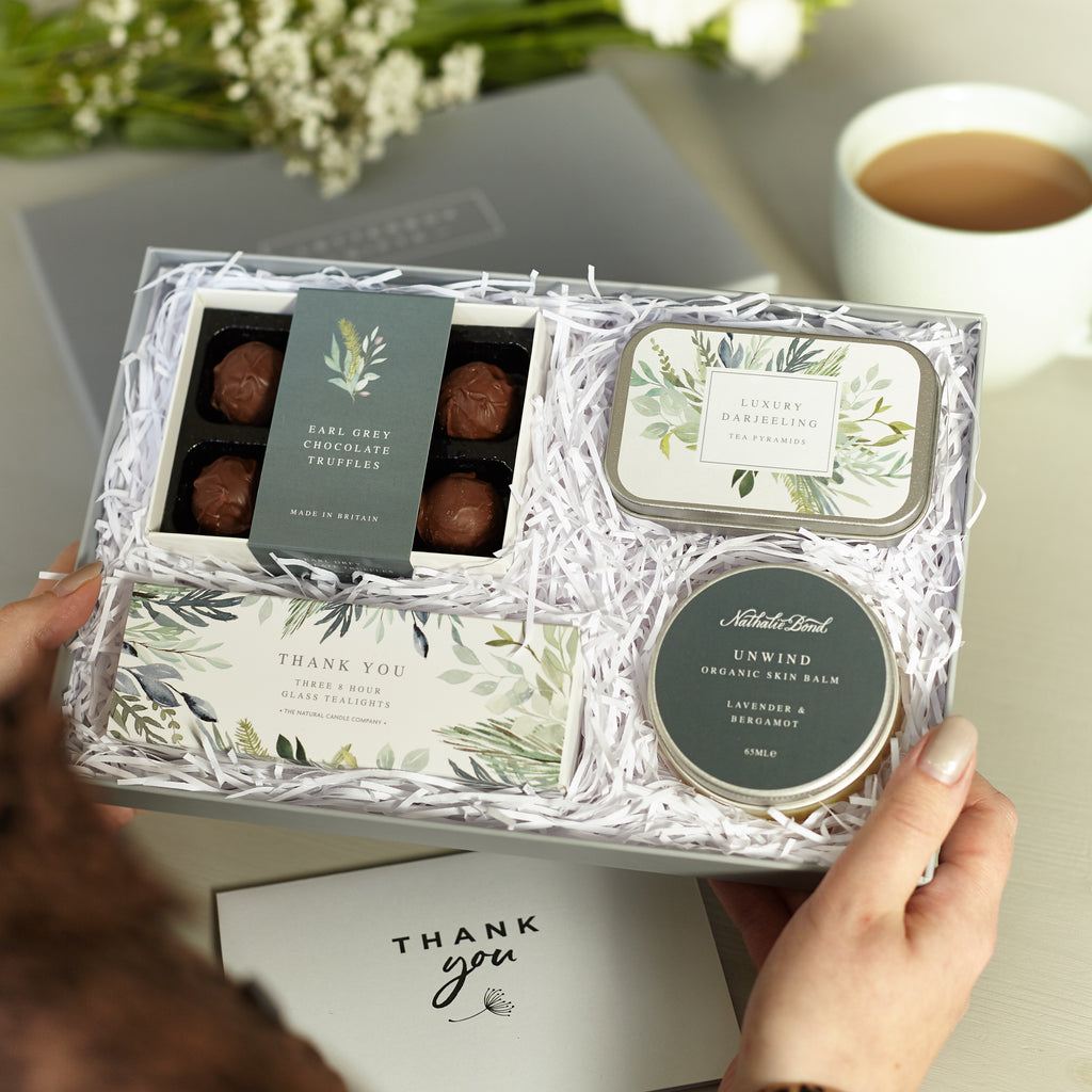 A person holding a Thank You letterbox gift set containing earl grey chocolate truffles, darjeeling tea tin, unwind skin balm & thank you tealights