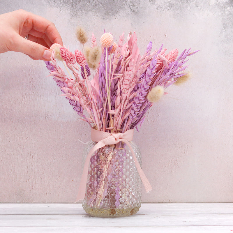 Pastel pink, purple and natural dried flower bouquet arranged in a glass jar with pink ribbon