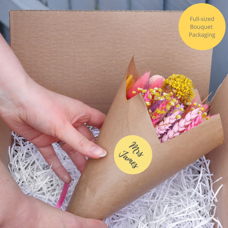 Full-sized summer dried flower bouquet being placed into straw packaging for postage