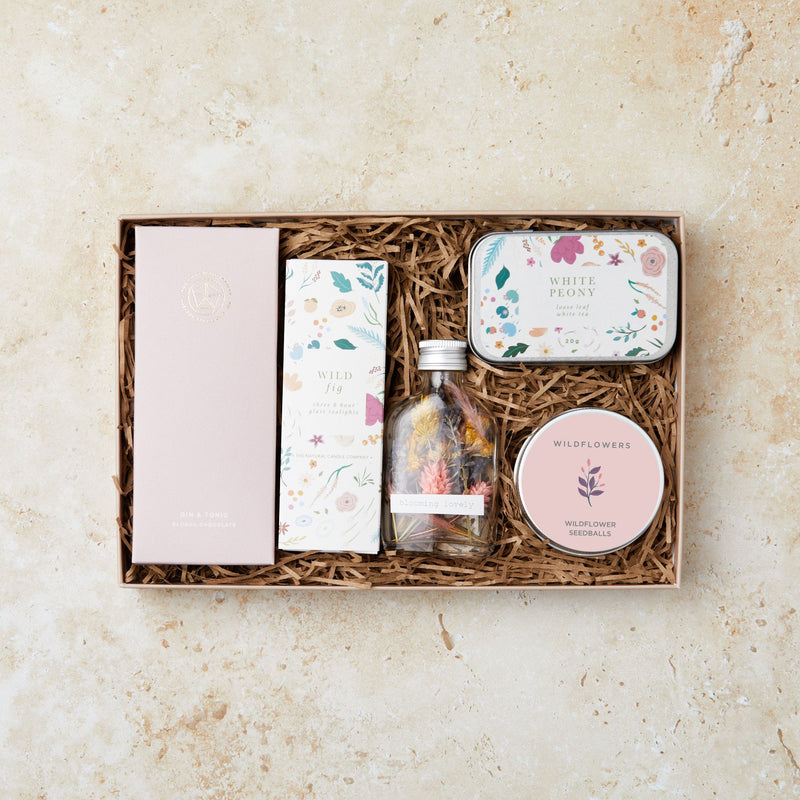 Letterbox gift set containing gin & tonic chocolate bar, wild fig tealights, white peony tea tin, wildflower seedballs and dried flowers in a glass bottle