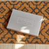 Grey letterbox gift set being delivered onto an orange and black doormat