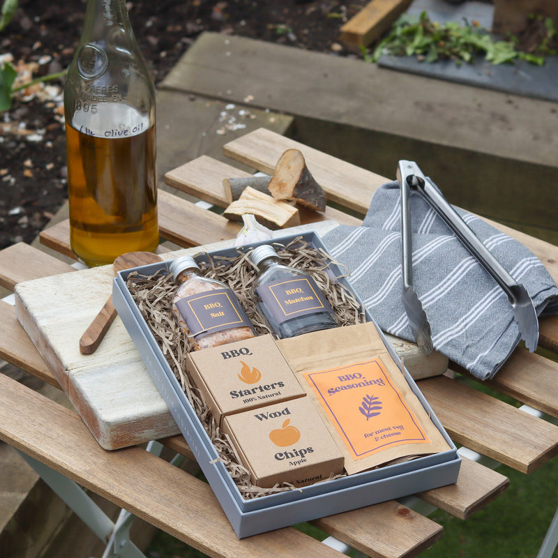 BBQ letterbox gift set outside on a table with BBQ tongs and bottle of olive oil