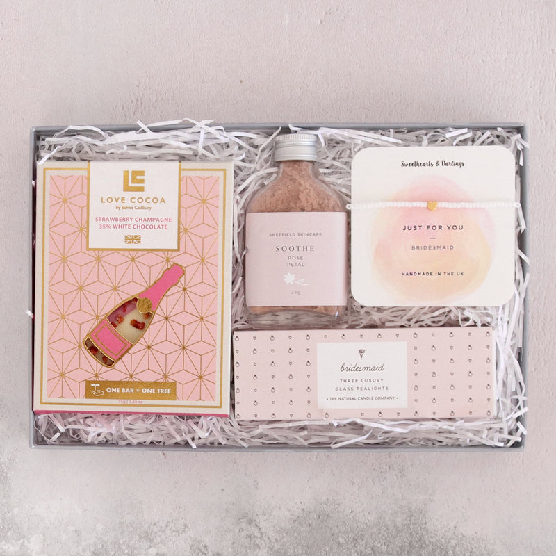 Bridesmaid letterbox gift set in pink, containing strawberry champagne chocolate bar, pink rose petal face mask, gold heart bead bracelet and bridesmaid tealights
