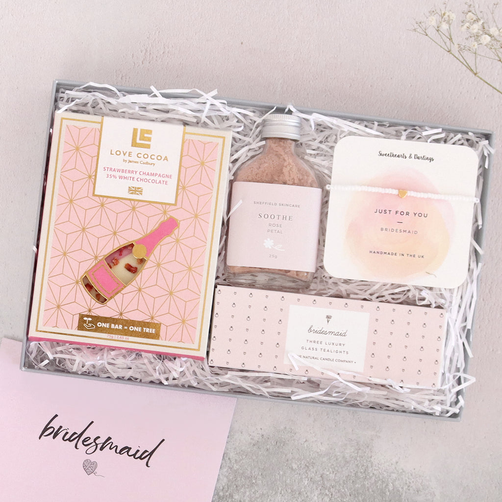 Bridesmaid letterbox gift set in pink, containing strawberry champagne chocolate bar, pink rose petal face mask, gold heart bead bracelet and bridesmaid tealights