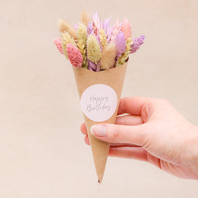 A person holding a pink & purple pastel dried flower posy with happy birthday sticker
