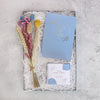 top view of an engagement gift set containing a posy of dried flowers, a wedding planner notebook and a box of Darjeeling tea in biodegradable pyramids