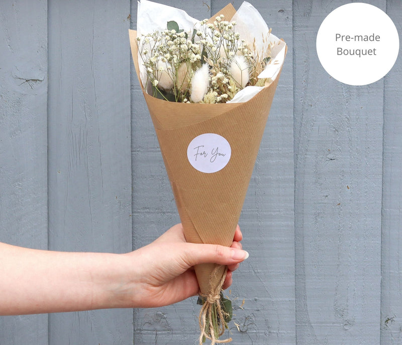 A person holding a pre-arranged full size neutral-tone dried flower bouquet in Kraft cone with for you sticker