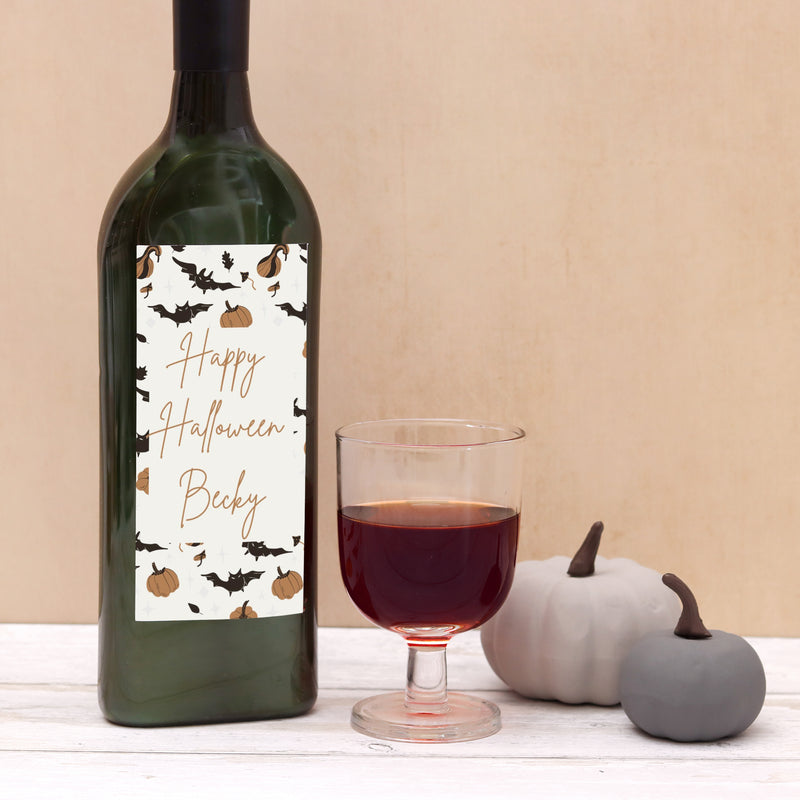 Letterbox wine bottle with personalised name on a happy halloween label with bat and pumpkin images next to glass of red wine