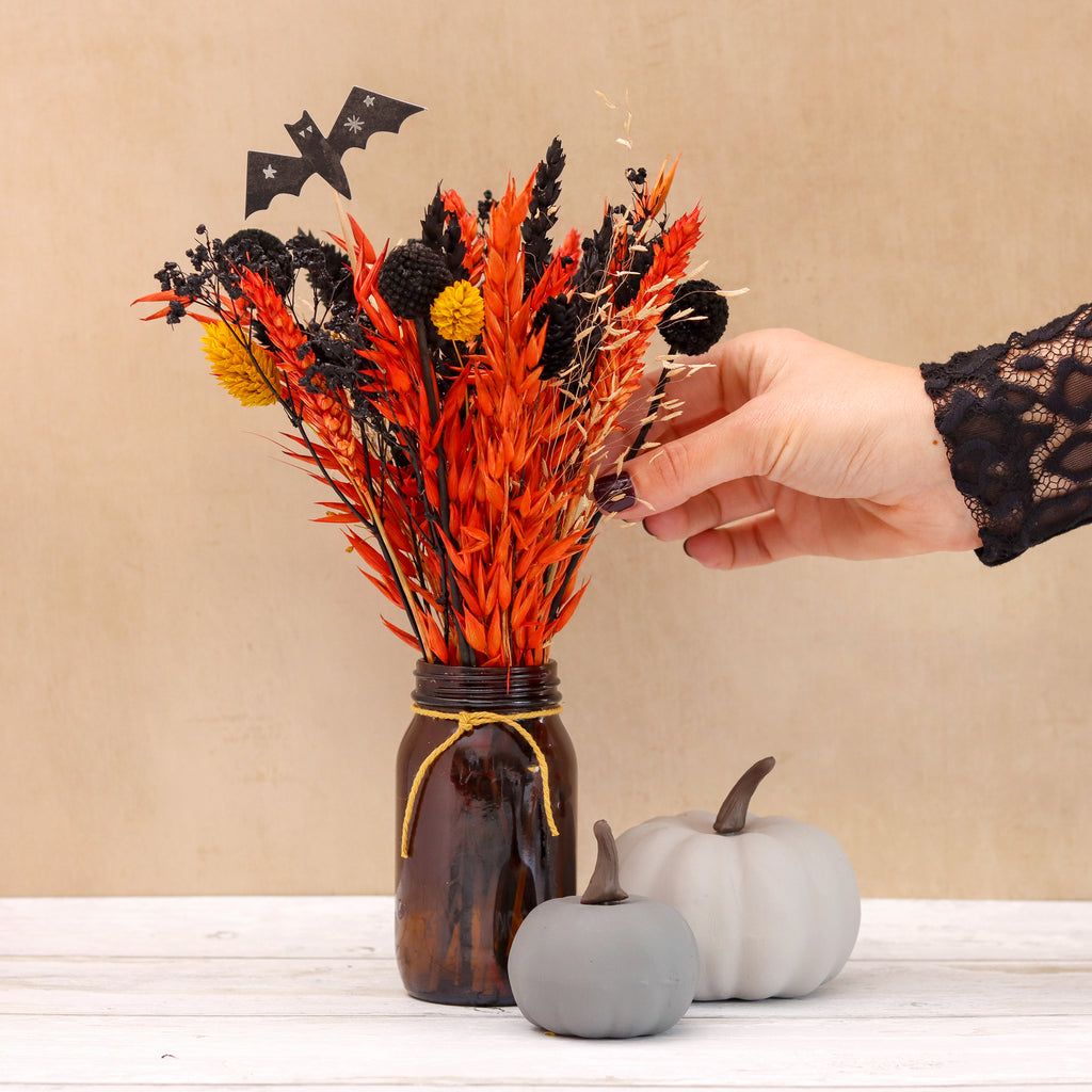 Orange, yellow and black halloween dried flower bouquet with black bat in brown glass jar