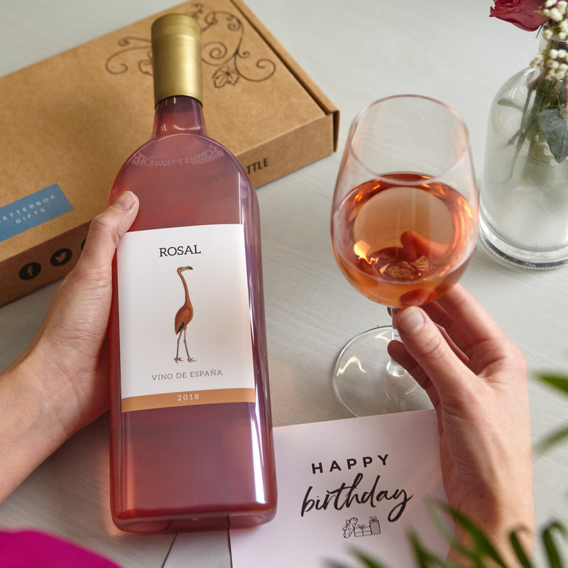 A person holding a glass of rose wine next to their letterbox-friendly rose wine bottle