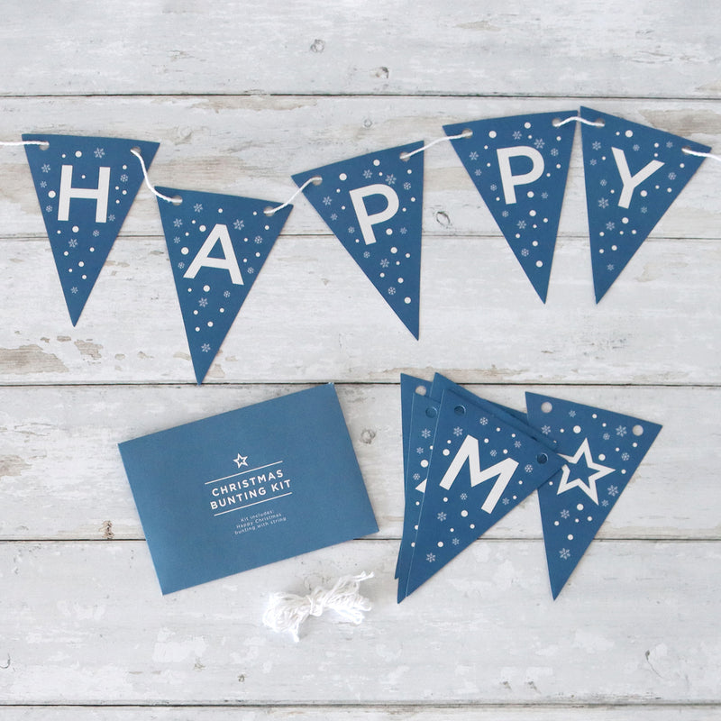 Blue and white 'happy christmas' bunting with snowflakes next to a bunting kit envelope