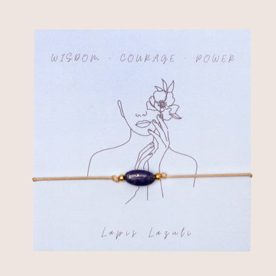 Lapis lazuli gemstone bracelet on a pastel blue card detailing the qualities of wisdom, courage and power