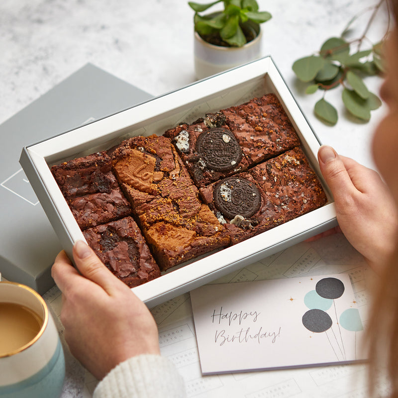 A person holding their letterbox-friendly chocolate brownie gift box with a happy birthday greetings card