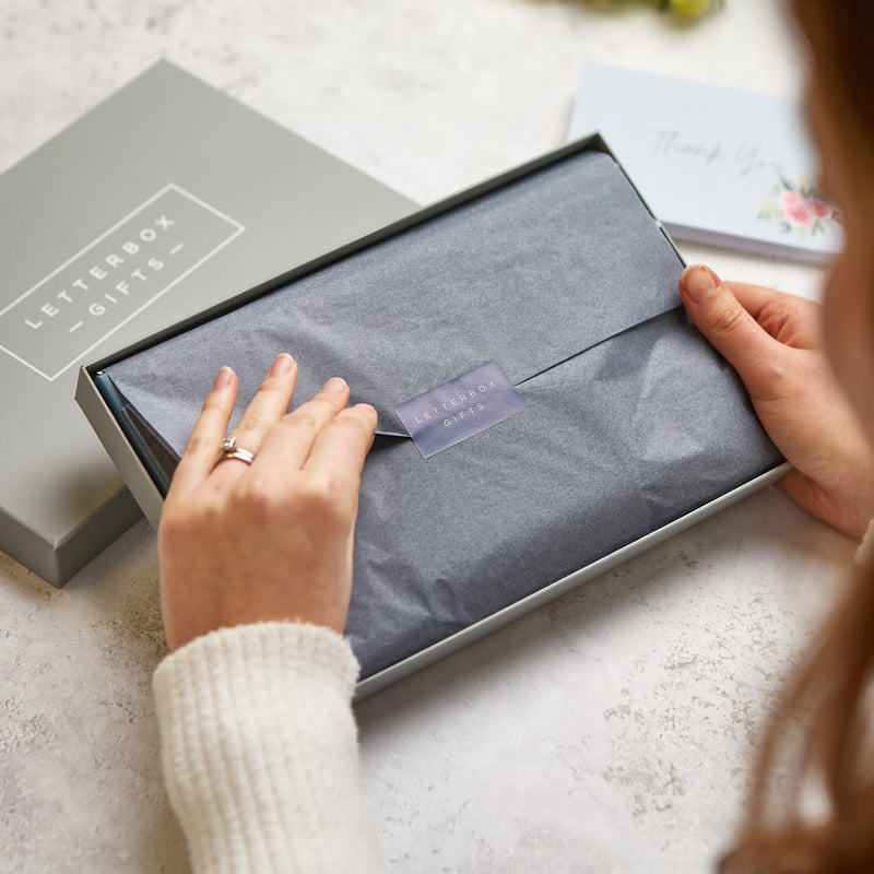 a woman opening grey gift wrapping of a gift box, with the letterbox box gifts logo on a central sticker.
