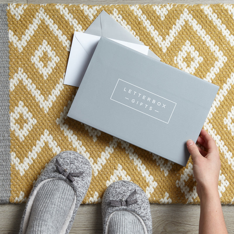A person picking up a grey letterbox gift box from their doormat 