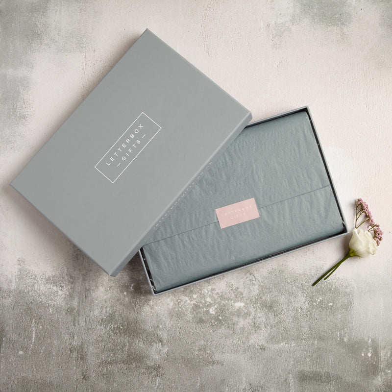 An open letterbox gift set showing the neatly wrapped grey tissue with pink Letterbox Gifts sticker