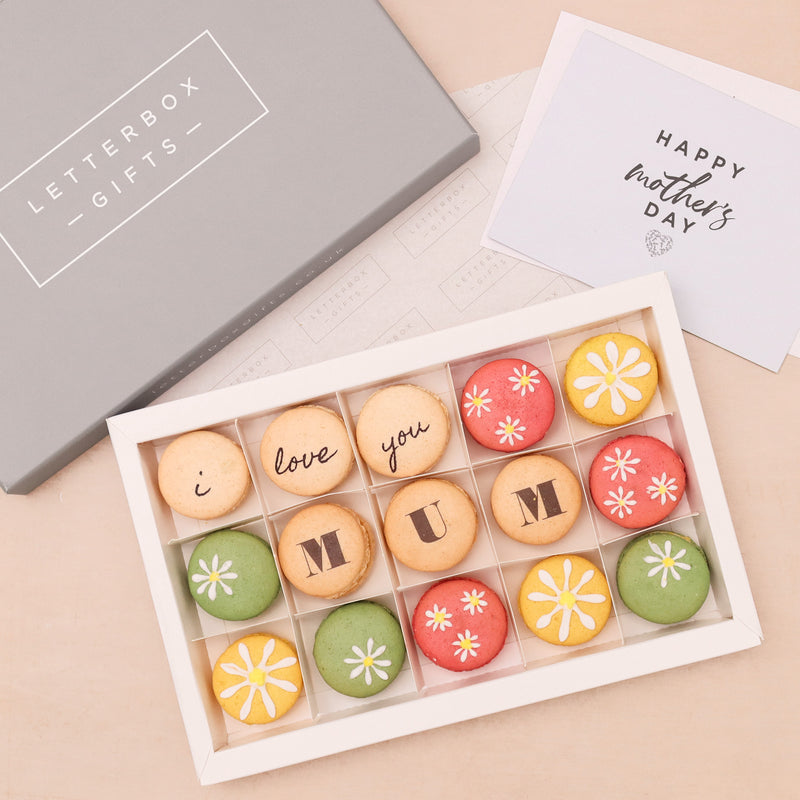 Fifteen mother's day macarons in pastel pink, green, yellow and cream, with 'i love you mum' printed text and white daisies