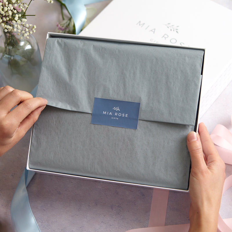 A person opening the neatly wrapped grey tissue on their new mum luxury gift hamper
