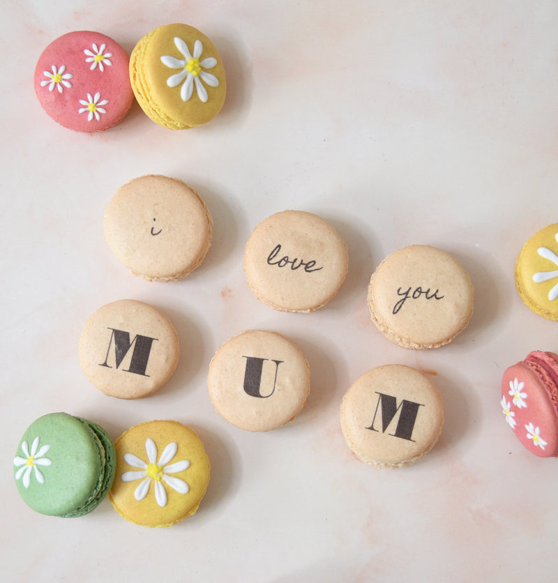 Fifteen hand-decorated colourful macarons with 'i love you mum' text and daisy flowers