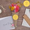 Bright summer dried flower posy in a Kraft cone with for you sticker, next to a thank you greetings card