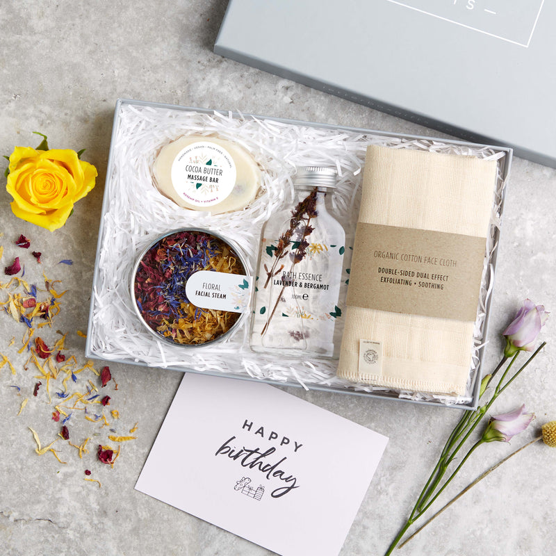 Eco friendly spa gift set containing organic cotton face cloth, bath essence, floral facial steam tin and cocoa butter massage bar