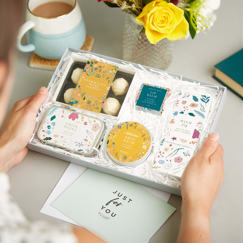 Botanical letterbox gift set containing sparkling wine truffles, lip balm, wild fig tealights, white peony tea & skin balm in bright floral design
