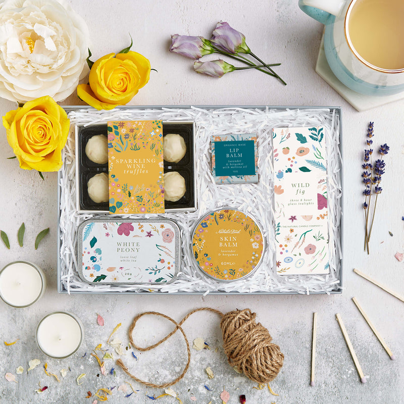 Botanical letterbox gift set containing sparkling wine truffles, lip balm, wild fig tealights, white peony tea & skin balm in bright floral design