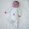 A baby lying on a bed wearing a white polar bear baby grow
